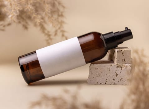 Brown glass cosmetic bottle with blank label on stones near pampas grass on light yellow, close up, mockup. Skincare beauty product. Natural eco friendly cosmetics