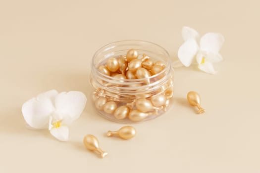 Beauty serum capsules in a jar near white orchid flowers on light yellow close up. Skincare cosmetics. Facial treatment with perfect dosage of serum to be used. Pastel composition..