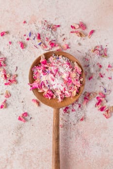 See salt wih with dried flower petals in wooden scoop on pink marble table