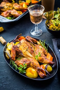 Baked whole chicken with potatoes, carrots, herbs and salt and rose wine on black background