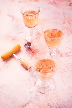 Three glasses of rose wine at wine tasting with bottle opener on pink marble background