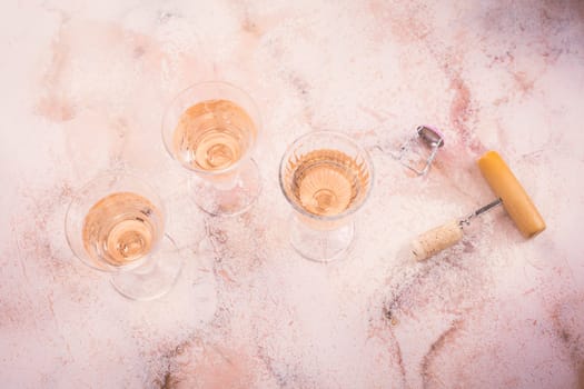 Three glasses of rose wine at wine tasting with bottle opener on pink marble background