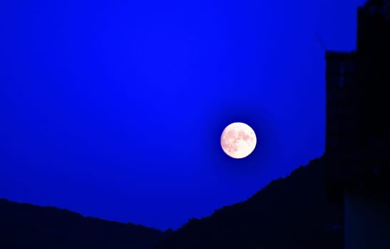 The moon rises behind a mountain