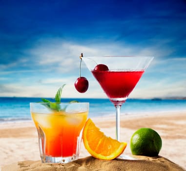 Cherry cocktail in martini glass and orange juice vodka on tropical sandy beach. Summer holiday and beach party design.