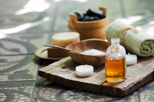 Natural spa settings and products on wooden plank. Sea salt, massage aromatic oils, towel, candles, spa stones and handmade soap in vintage bathroom. Aromatherapy concept.