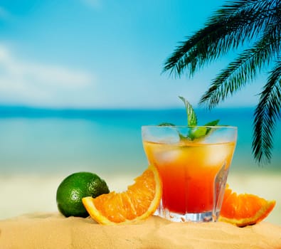 Orange cocktail and citrus fruit on tropical sandy beach. Summer holiday and beach party design.