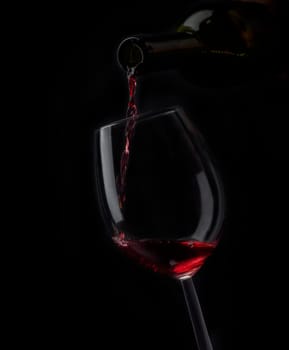 Red wine pouring in wineglass from bottle over black background. Wine list design menu with copyspace. Alcohol beverage card backdrop.