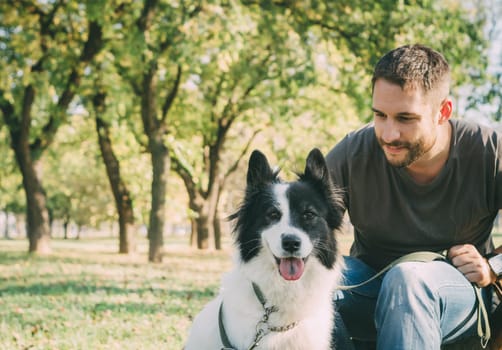 Man with his dog playing outdoor in the park. Young owner hugs his pet in nature.