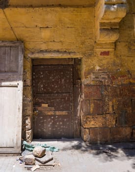 Broken wooden brown door on grunge stone bricks wall painted in orange in abandoned Darb El Labana district, Cairo, Egypt