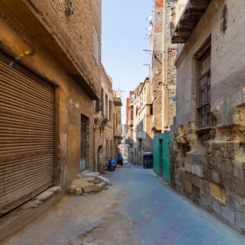 Aged houses with crumbling walls located on narrow abandoned street on sunny day in old Cairo, Egypt