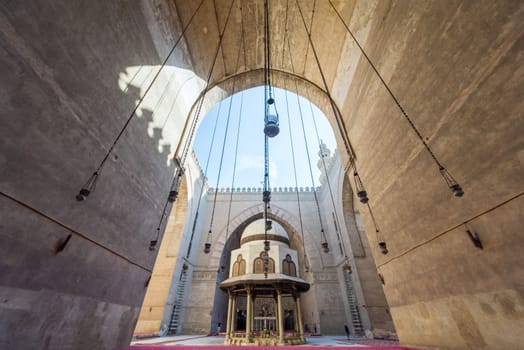 Cairo, Egypt - December 16, 2017: Courtyard of the Mosque of Sultan Hasan with Ablution fountain and huge arch, and few tourists visiting the place at the early morning