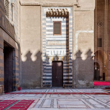 Wall with striped black and white marble decorations, wooden grunge door and window at the courtyard of historic public mosque of Sultan Hassan, Cairo, Egypt