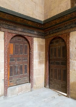 Two wooden aged ornate vaulted perpendicular doors on stone bricks walls, Medieval Cairo, Egypt