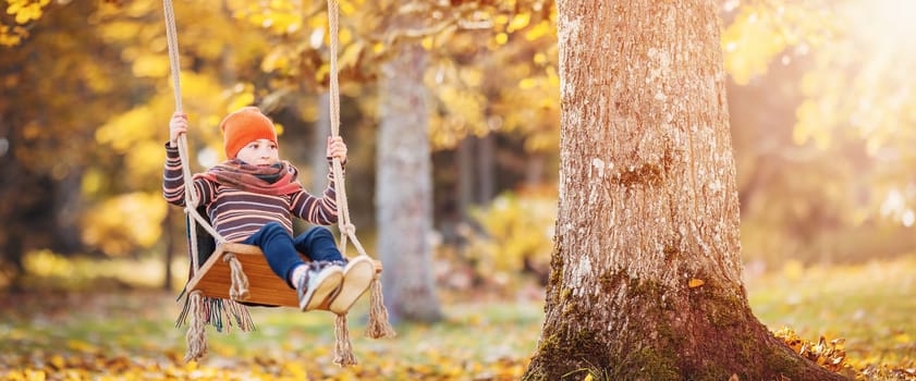 Happy girl sitting on the swing in autumn natural park. Concept of childhood.