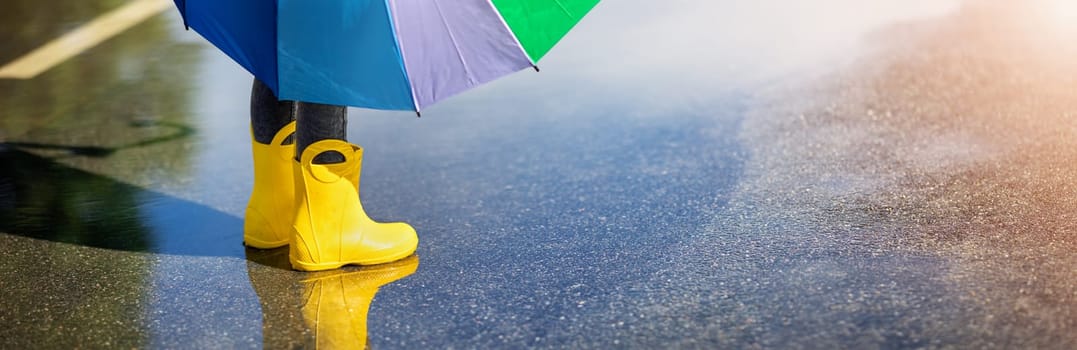 Child standing in the puddle in yellow rubber boots. Concept of childhood.