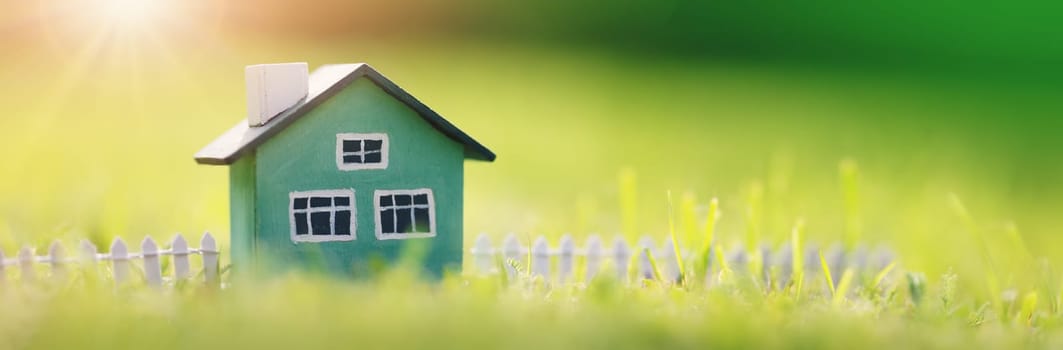 Green house model with fence standing on the green grass. Panoramic view. Conceptual symbol of the buying a new house or ownership of real estate.