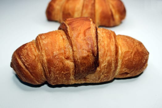 Fresh crispy croissant close-up on a light background. Blurred croissant in the background. Cooking, home baking.