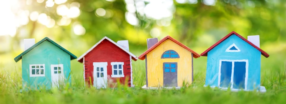Several colourful houses models standing on the green grass. Panoramic view. Conceptual symbol of the buying a new house or ownership of real estate.