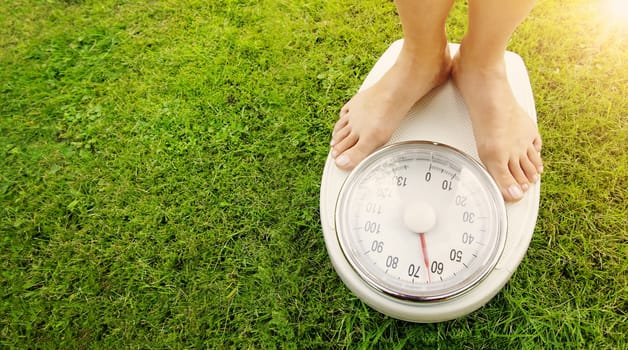 Woman standing on the white scales with bare feet in nature. Concept of the weight loss and healthy lifestyle.