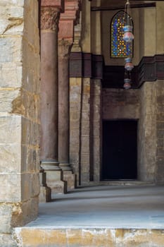 Passage at Sultan Qalawun Mosque with stone columns, colored stained glass windows and wooden door, Cairo, Egypt