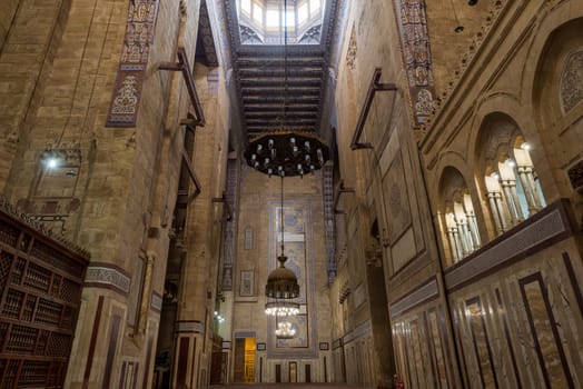 Interior of al Refai mosque with old decorated bricks stone wall, colored marble decorations, wooden ornate ceiling, big brass chandeliers, and wooden latticework door, Cairo, Egypt