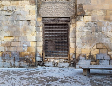 Wooden window with decorated iron grid over stone bricks wall and marble garden bench, Moez Street, Cairo, Egypt