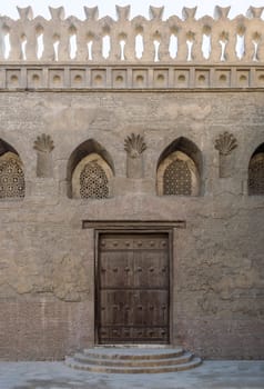 Aged wooden weathered door, perforated arched stucco window decorated with floral patterns, and three steps on stone bricks wall, Ibn Tulun Mosque, Cairo, Egypt