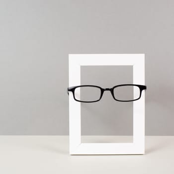 Home interior poster mock up with wooden frame and eyeglasses, gray wall background, copy space for text and pictures