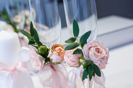 Two gold wedding rings close up lie on flowers decorating champagne glasses. Wedding details, symbol of love and marriage. Beautiful wedding background.