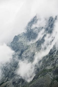 A mystical photo of rough rocky mountains surrounded by a white blanket of clouds