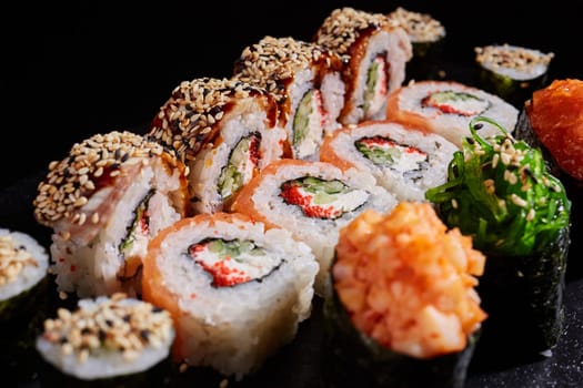 Close up of delicious sushi rolls with cucumber, avocado, fish caviar and sesame seeds on dark background. Japanese oriental cuisine. Concept of delivery of delicious original sushi sets.