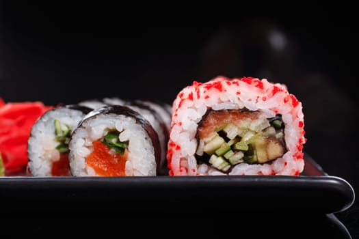 Rice Japanese rolls of Uramaki and Maki with salmon, cucumber, and red caviar on a black plate. Traditional Japanese food. Close-up.