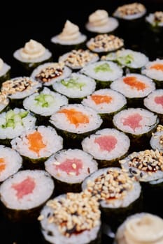 Large set of Maki rolls with a variety of fresh fish and vegetable fillings. Rolls with cream cheese, salmon, cucumber, sesame seeds and sauce. Selective focus.