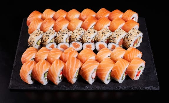 Sushi set which consists of a large number of roles of Philadelphia with raw salmon and other sushi in between. Japanese sushi set. Different types of rolls on a stone plate on a black background.