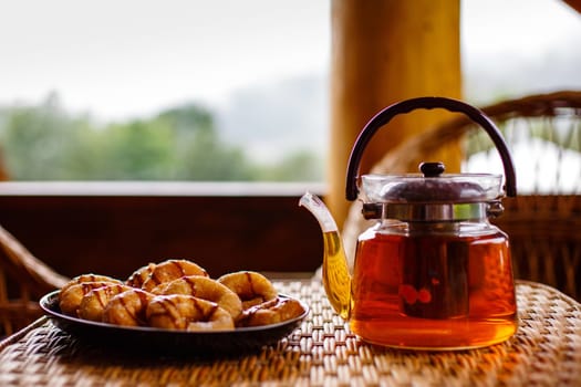 Close up breakfast in nature with herbal tea in a glass teapot and pastries on a plate on the table. Morning rituals. Blurred background. Selective focus.