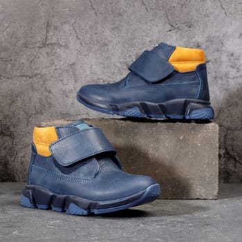 Blue winter sports shoes with orange inserts and velcro for men on a gray concrete background. Boots for the winter and autumn seasons.