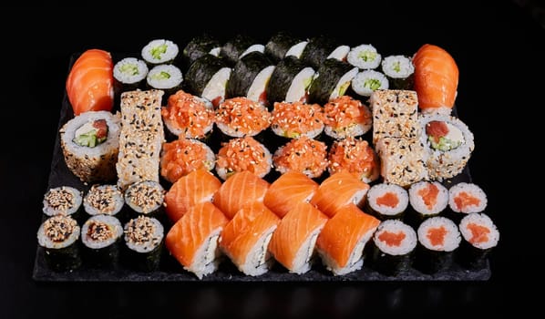 Assortment of different types of sushi rolls placed on a black stone board. Menu sushi with nigiri, maki, uramaki for ordering in a restaurant or delivery. Japanese Oriental Cuisine.