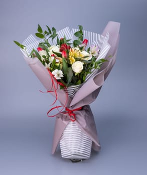 Flower bouquet, which is wrapped in light floral paper of two types stands on a blue background. Bouquet of white roses, colored irises and red tulips. Concept of floral arrangements for greetings.