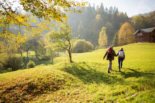 Active tourism. Rear view of a young couple of travelers who lead an adventurous lifestyle and travel in the mountains go to a wooden house to relax. Concepts about travel, lifestyle and wanderlust.
