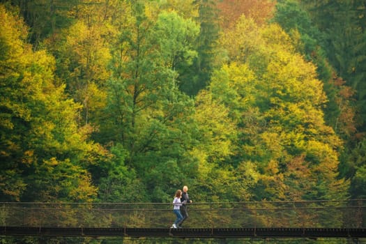 Early morning workout. Young sports family performs a morning jog on a suspension bridge against the backdrop of a mountain forest. Concept of active and healthy lifestyle. Mountain forest landscape.