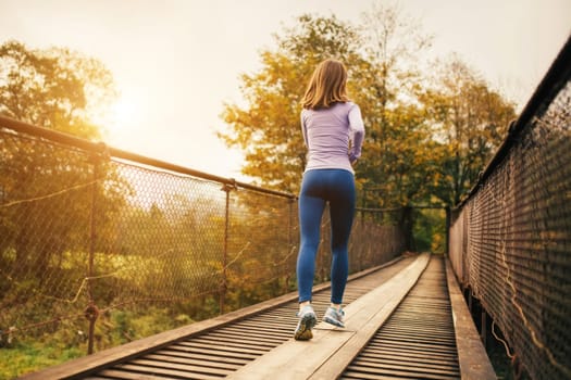 Morning sports run. Rear view of a young female athlete jogging in the morning on the bridge. Female fitness athlete practicing jogging outdoors. Concept of a healthy lifestyle.