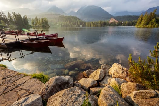View of a mountain lake Strbske pleso in the High Tatras. Slovakia. Boats on the water glow in the sun at sunrise.