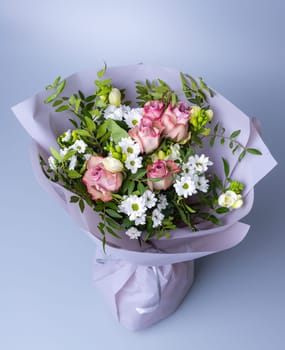 Top view of a bouquet of roses and green twigs on a blue background. Festively packed bouquet with pink roses, white chrysanthemums and sprigs of greenery. Floristics concept.