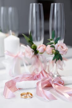 Wedding accessories. Rings and wedding details in pink style, which are on the table. Wedding rings lie on the table near the candles with pink ribbons and glasses decorated with pink flowers.