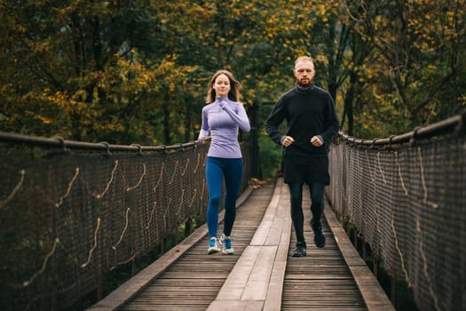 Early morning workout. Young athletic man and woman performing a morning run on a suspension bridge. Athletes in sportswear train outdoors. Healthy lifestyle.