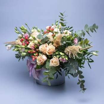Festively packaged bouquet in pastel color composed of roses, other different flowers and sprigs of greenery on a blue background. Background for greetings and postcards. Floral banner.
