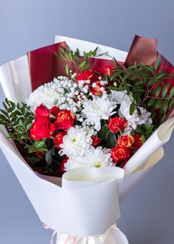 Floral arrangements. Close up of white and red flowers wrapped in bright floral paper on blue background. Bouquet of pink roses, white chrysanthemums, gypsophila and sprigs of greenery.