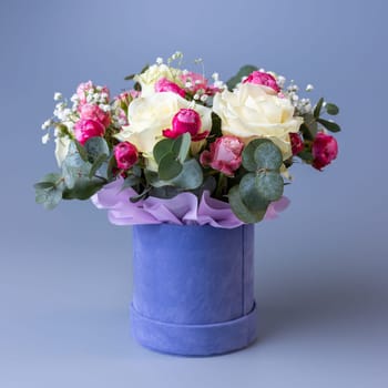 Delicate holiday bouquet in a blue velor round gift box on a blue background. Bouquet with beige and pink roses, white gypsophila and eucalyptus twigs. Concept of Women's Day, Mother's Day and Birthday.