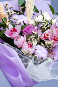 Close up of floral bouquet of fresh natural ingredients wrapped in floral tracing paper. Festively packaged bouquet in pink style composed of irises, other different flowers and twigs of cotton.