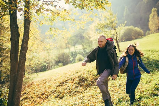 Portrait of happy and joyful man and woman hikers running holding hands on mountain terrain. Guy and girl travel together. Concepts about travel, lifestyle and wanderlust.